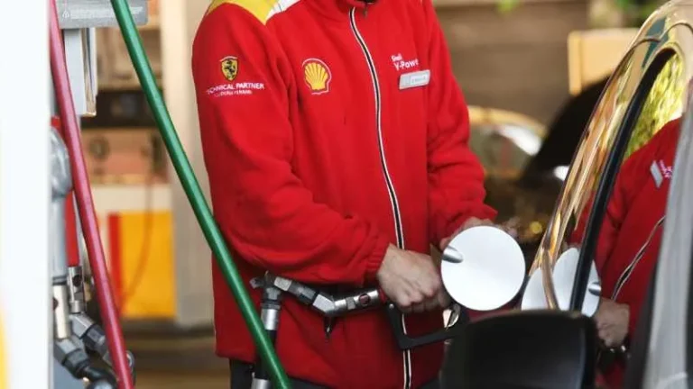 Gráfico de precios de combustibles y un surtidor de nafta en una estación de servicio.