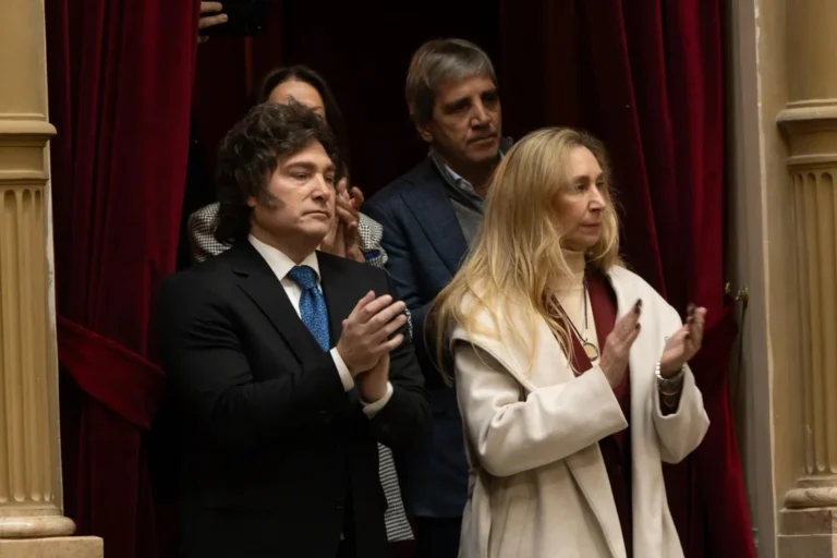 Javier Milei mirando su teléfono con gesto serio, rodeado de iconos de redes sociales